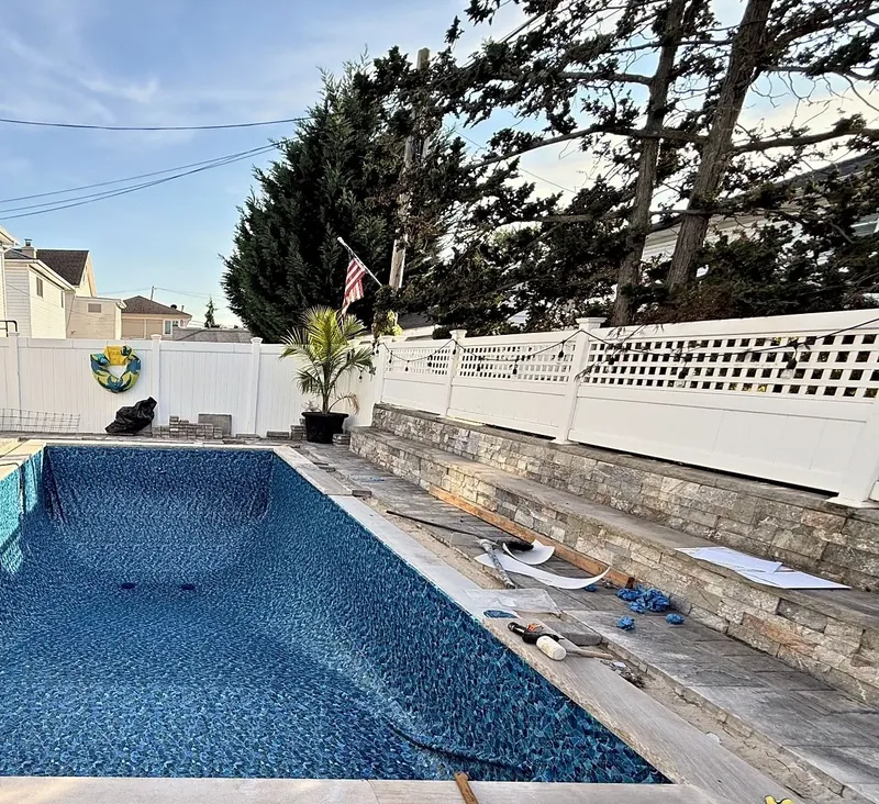 Mosaic-pattern liner installed and stone coping set beside the stacked-stone wall