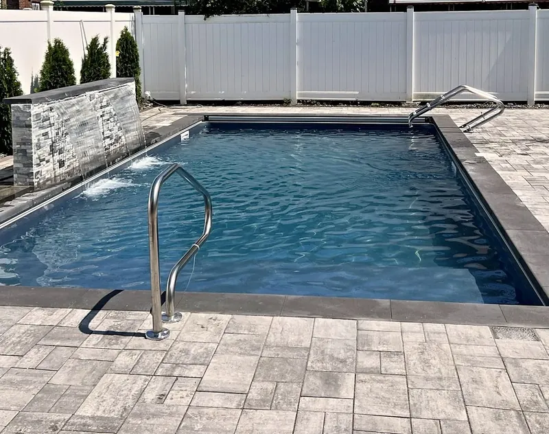 Pools – Build, Repair & Service – Finished pool with stacked-stone waterfall, dark coping and stainless entry rail